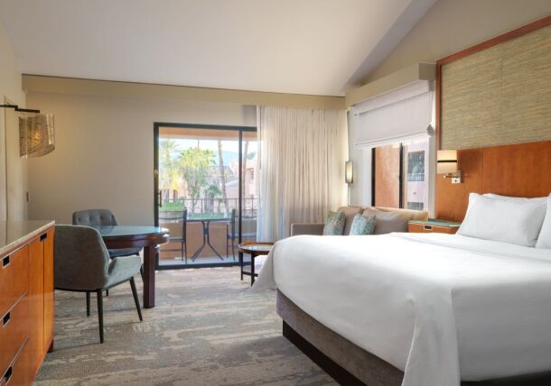 View of hotel room with bed, bureau, and table, with outdoor balcony